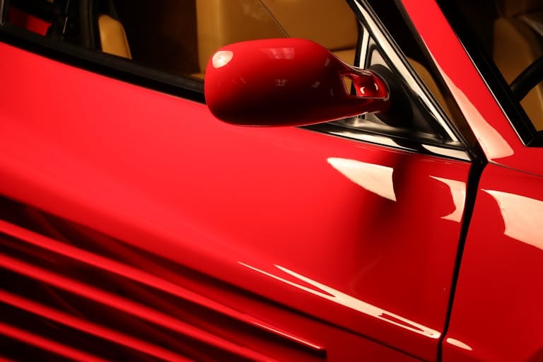 Red Ferrari Testarossa side mirror detail shot showcasing luxury design elements.